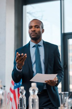 Elinde kağıt tutarken işaret eden yakışıklı Afrikalı Amerikalı diplomatın seçici odak noktası 