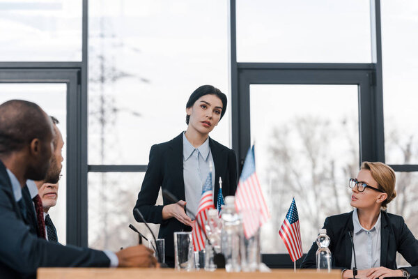 избирательное внимание привлекательного докладчика, говорящего рядом с мультикультурными дипломатами и американскими флагами
 