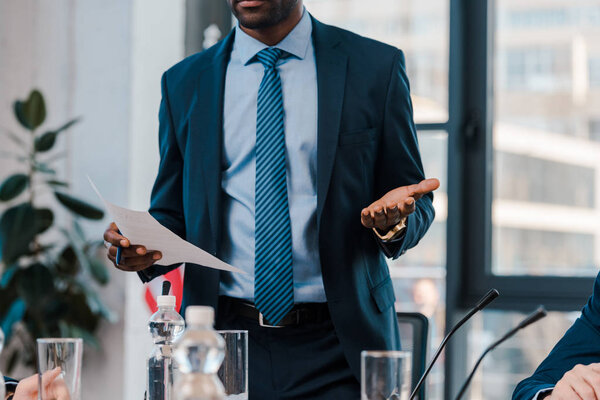 обрезанный взгляд на африканского американского дипломата жестикулируя, держа в руках бумагу
 