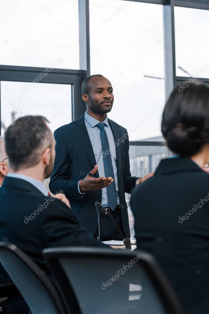 selective focus of african american diplomat in formal wear gesturing near businessmen and businesswoman 