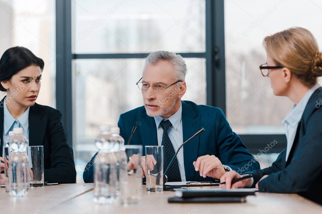 selective focus of attractive businesswomen looking at bearded diplomat 