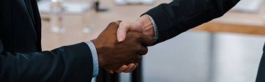 panoramic shot of businesswoman shaking hands with african american businessman  clipart