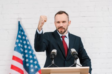 Duygusal konuşmacının seçici odağı yumruğunu sıkmış mikrofonlar ve Amerikan bayrağı önünde konuşuyor. 