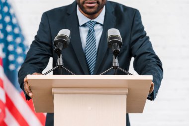 Afrika kökenli Amerikan konuşmacısının mikrofonların ve Amerikan bayrağının yanında konuşması. 