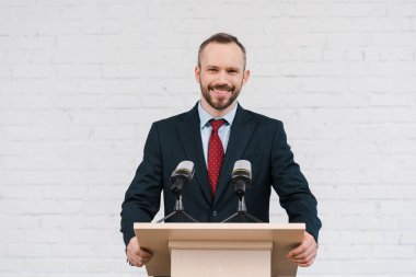 happy bearded speaker smiling near microphones and brick wall  clipart