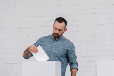 handsome voter putting blank ballot in voting box  clipart