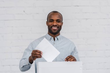 happy african american voter putting blank ballot in voting box  clipart