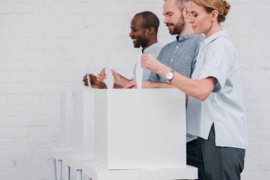 selective focus of happy multicultural citizens voting while standing near boxes  clipart