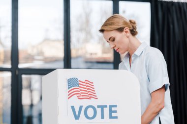 Oy pusulası ve Amerikan bayrağıyla oy veren çekici bir kadının yan görüşü 
