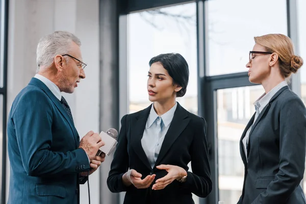 Guapo Hombre Negocios Sosteniendo Micrófono Cerca Hermosas Empresarias — Foto de Stock