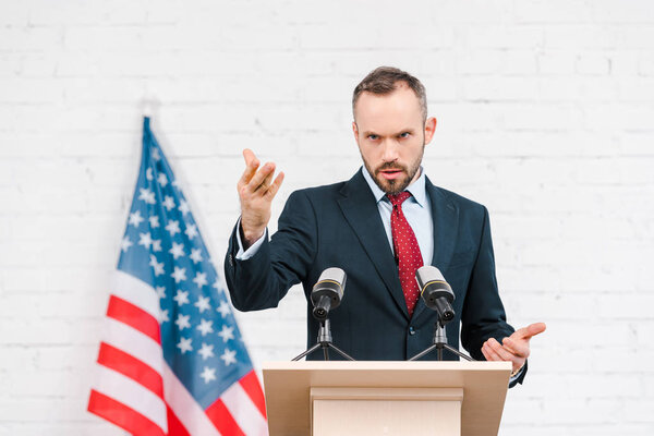 handsome speaker in suit gesturing while talking near microphones 