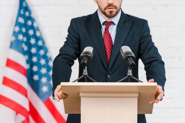 cropped view of bearded speaker in suit standing near microphones 