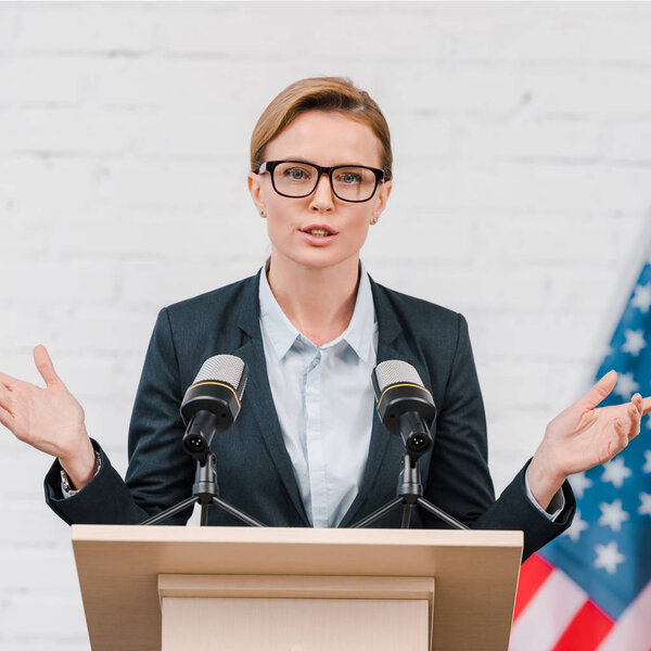 attractive speaker in glasses gesturing while talking near microphones 