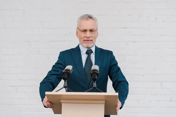 Glad Skäggig Högtalare Glas Talar Nära Mikrofoner Och Tegelvägg — Stockfoto