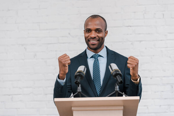 happy african american speaker standing with clenched fists near microphones 