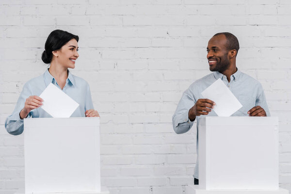 happy woman and african american man voting near brick wall 