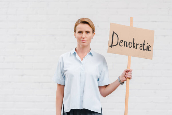 attractive woman holding placard with demokratie lettering near brick wall 