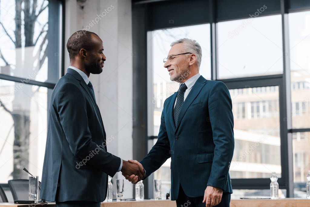 cheerful businessman shaking hands with african american diplomat 