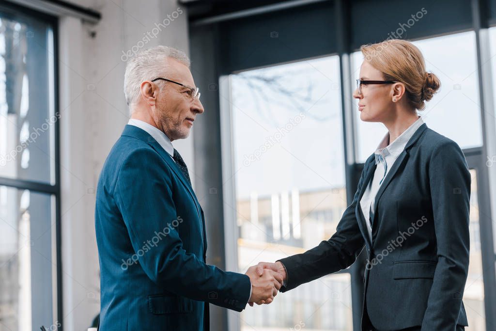 side view of businesswoman shaking hands with businessman in glasses 