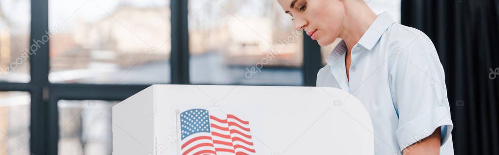 panoramic shot of attractive woman voting near stand with american flag 