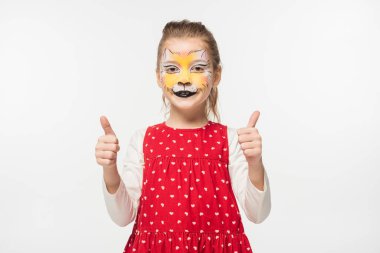 happy child with tiger muzzle painting on face showing thumbs up isolated on white clipart