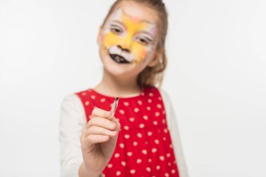 selective focus of adorable kid with tiger muzzle painting on face pointing with paintbrush at camera isolated on white clipart