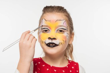 cute kid with tiger muzzle painted on face painting on eyebrow with paintbrush isolated on white clipart