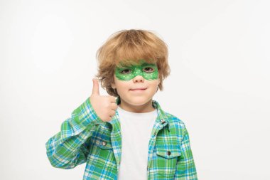 cheerful boy with gecko mask painted on face showing thumb up while looking at camera isolated on white clipart