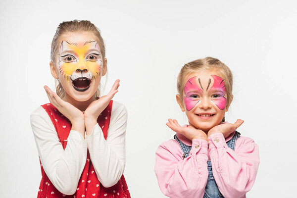 excited friends with cat muzzle and butterfly paintings on faces looking at camera isolated on white