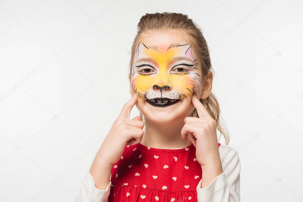 cheerful child with tiger muzzle painting on face touching face with fingers isolated on white