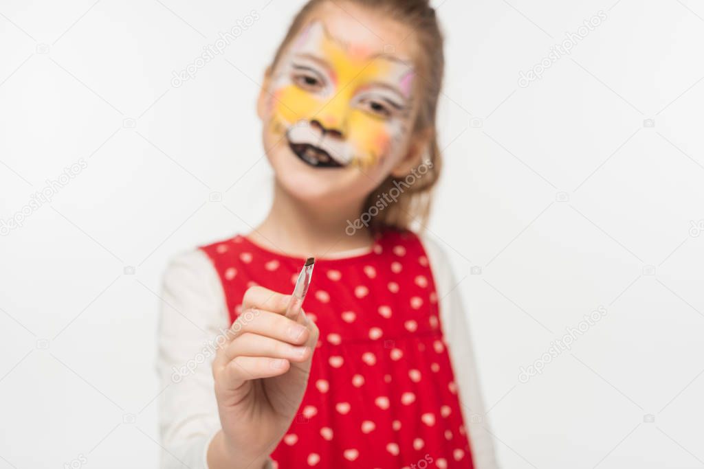 selective focus of adorable kid with tiger muzzle painting on face pointing with paintbrush at camera isolated on white
