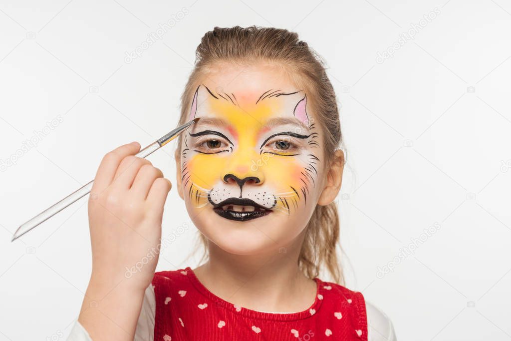 cute kid with tiger muzzle painted on face painting on eyebrow with paintbrush isolated on white
