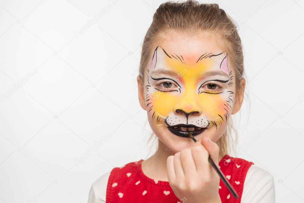 cute kid with painted tiger muzzle on face painting on lips with paintbrush isolated on white