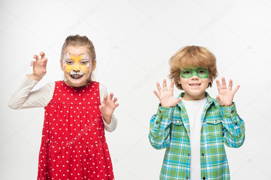 cheerful friends with cat muzzle and gecko mask paintings on faces showing frightening gestures at camera isolated on white
