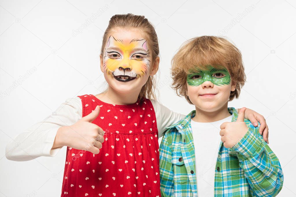 cheerful friends with cat muzzle and gecko mask paintings on faces showing thumbs up isolated on white