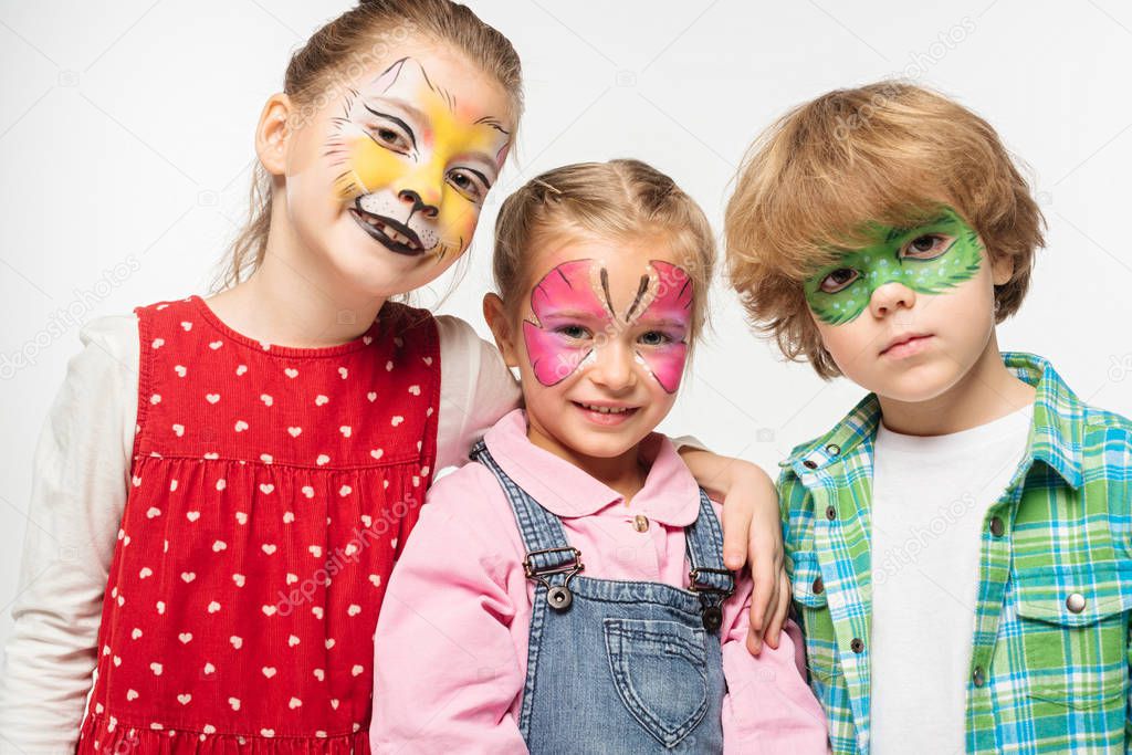 smiling friends with colorful face paintings looking at camera isolated on white