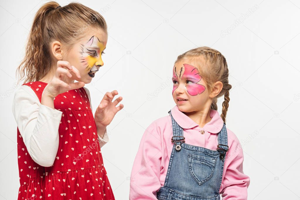 adorable kid with cat muzzle painting on face scaring friend isolated on white
