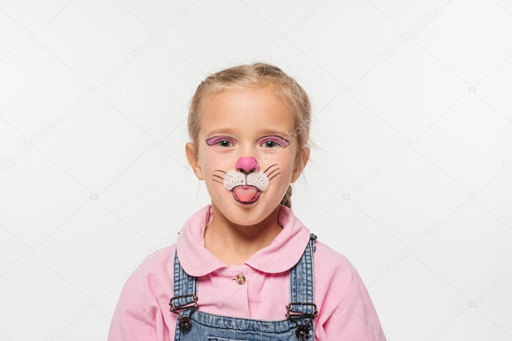 cheerful kid with cat muzzle painting on face sticking tongue out while looking at camera isolated on white