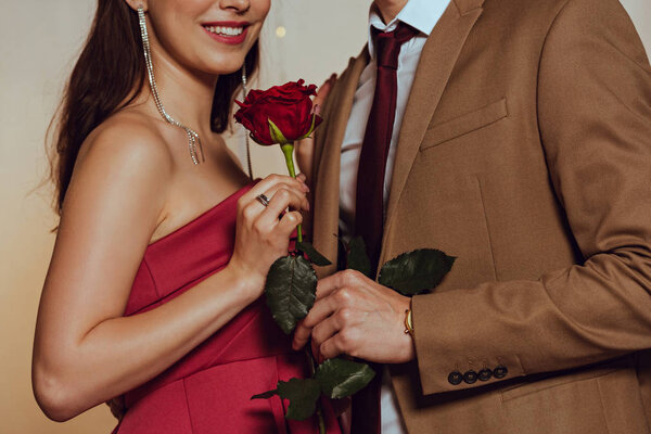 cropped view of smiling, elegant girl holding red rose while standing near boyfriend in restaurant