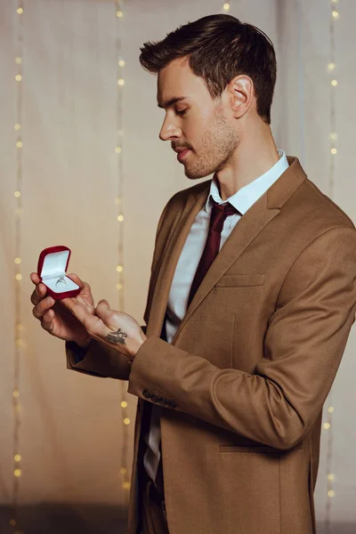 エレガントでハンサムな男がレストランに立っている間に結婚指輪付きの箱を持っている — ストック写真
