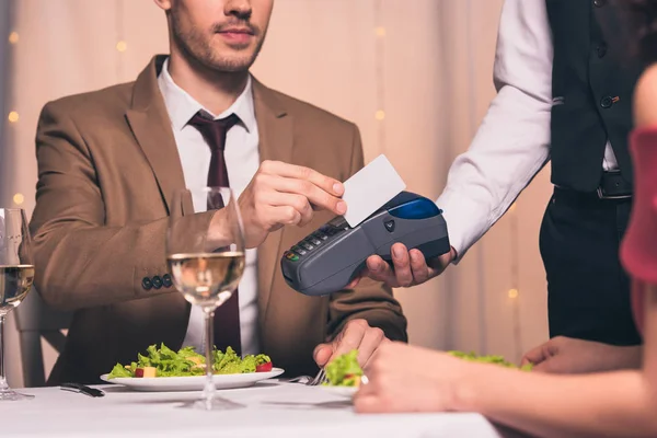优雅男子坐在靠近女朋友的餐馆用信用卡支付终端费的剪影 — 图库照片