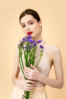 attractive woman holding purple limonium flowers isolated on beige 