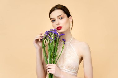 young beautiful woman holding purple limonium flowers isolated on beige 