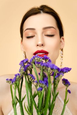 beautiful woman with closed eyes near purple limonium flowers isolated on beige 