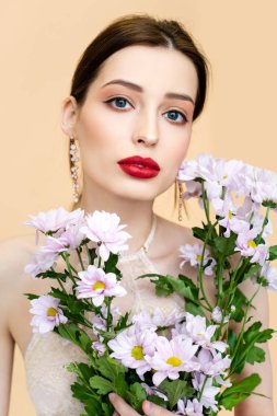 young woman holding blooming chrysantemum flowers isolated on beige 