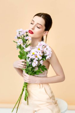 pretty woman with closed eyes holding blooming chrysanthemum flowers on beige 