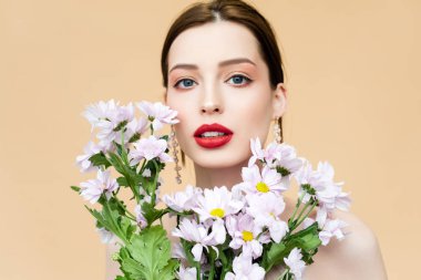 pretty girl looking at camera near blooming chrysanthemum flowers isolated on beige 