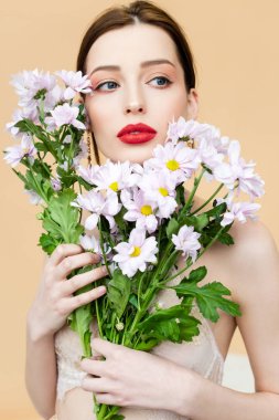 pretty girl looking away and holding blooming chrysanthemum flowers isolated on beige 