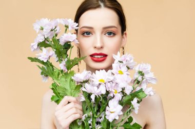 beautiful girl looking at camera and holding blooming chrysanthemum flowers isolated on beige 