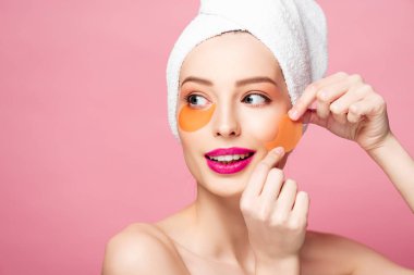 happy naked girl applying eye patches isolated on pink 